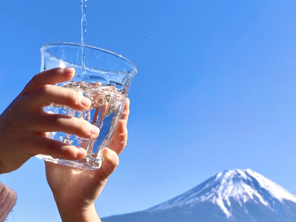 富士山を背景に水道水をコップに受ける写真