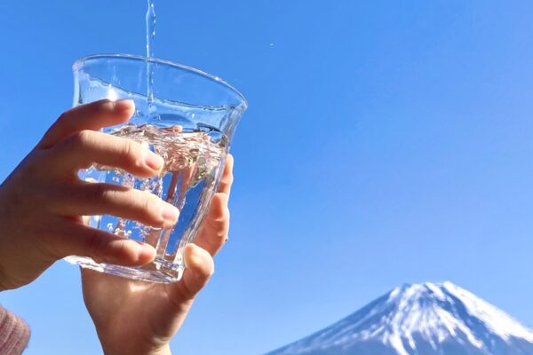 富士山を背景に水道水をコップに受ける写真